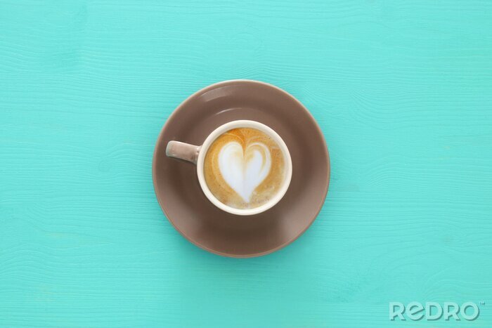 Canvas afbeelding van koffie beker met schuim van hartvorm over houten blauwe tafel.