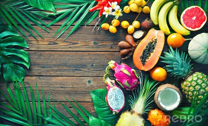 Canvas Assortiment van tropische vruchten met bladeren van palmbomen en exotische planten op donkere houten achtergrond