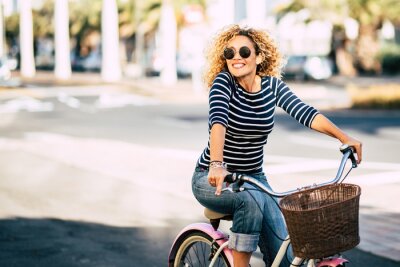 Canvas Beautiful and cheerful adult young woman enjoy bike ride in sunny urban outdoor leisure activity in the city - happy people portrait - trendy female outside having fun