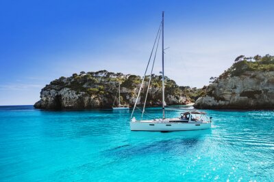Canvas Beautiful beach with sailing boat yacht, Cala Macarelleta, Menorca island, Spain. Yachting, travel and active lifestyle concept	