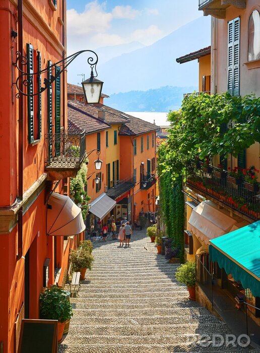 Canvas Bellagio village at lake Como near Milan Italy, region Lombardy. Famous street with paving stones stairs and cosy restaurants during sunrise with glowing lanterns and green plants on old houses walls.