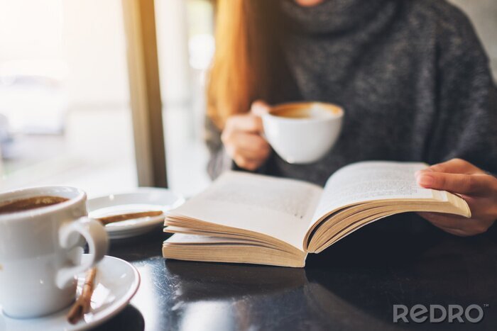 Canvas Closeup image of a woman reading a book while drinking coffee in cafe