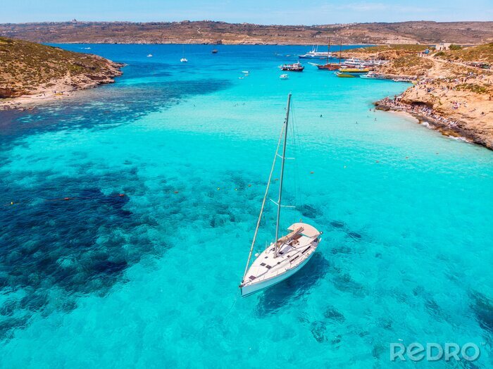 Canvas Concept paradise vacation. White yacht with sail in clear water of sea with sand. Blue Lagoon Comino Malta. Aerial view