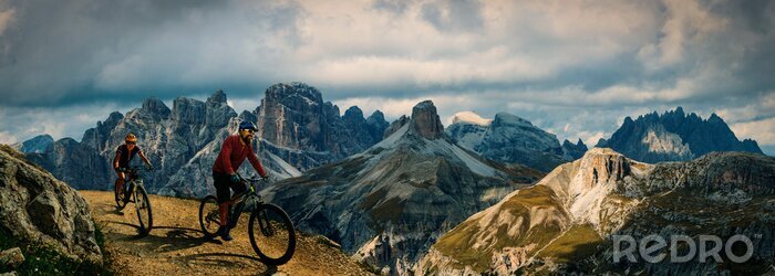 Canvas Cycling outdoor adventure in Dolomites. Cycling woman and man  on electric mountain bikes in Dolomites landscape. Couple cycling MTB enduro trail track. Outdoor sport activity.