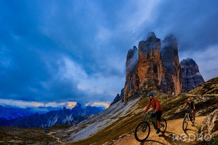 Canvas Cycling outdoor adventure in Dolomites. Cycling woman and man  on electric mountain bikes in Dolomites landscape. Couple cycling MTB enduro trail track. Outdoor sport activity.
