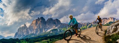 Canvas Cycling woman and man riding on bikes in Dolomites mountains andscape. Couple cycling MTB enduro trail track. Outdoor sport activity.
