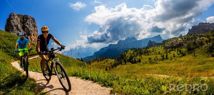 Canvas Cycling woman and man riding on bikes in Dolomites mountains landscape. Couple cycling MTB enduro trail track. Outdoor sport activity.