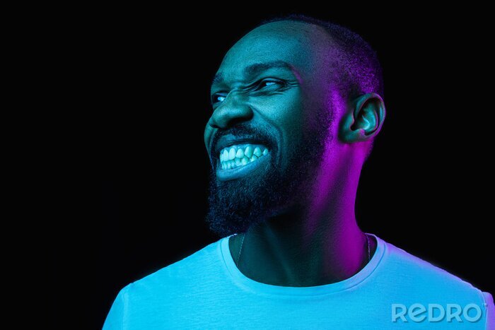 Canvas De retro wave of synth wave portret van een jonge gelukkig lachende Afrikaanse man in de studio. High Fashion mannelijk model in kleurrijke heldere neonlichten die op zwarte achtergrond stellen. Art o