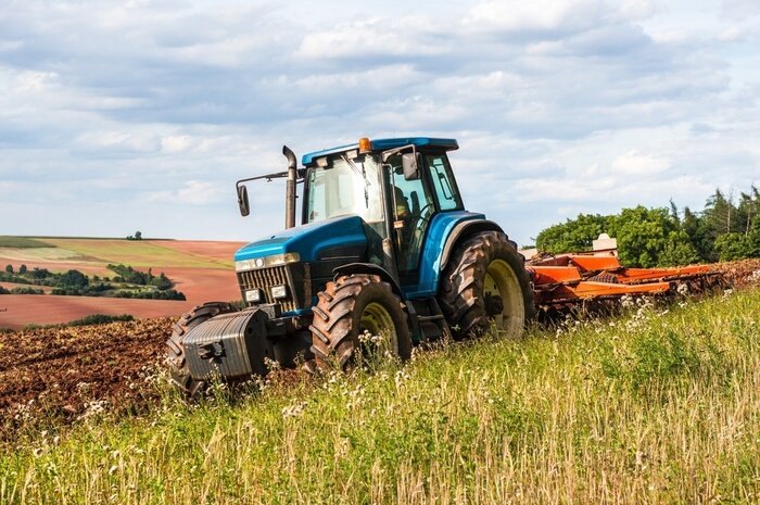 Canvas Een blauwe tractor aan het werk op een veld op een heldere dag.