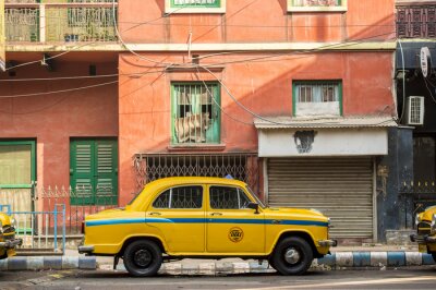Canvas Een gele taxi van de ambassadeur staat geparkeerd op straat onder een roodgekleurd huis in Kolcata, India
