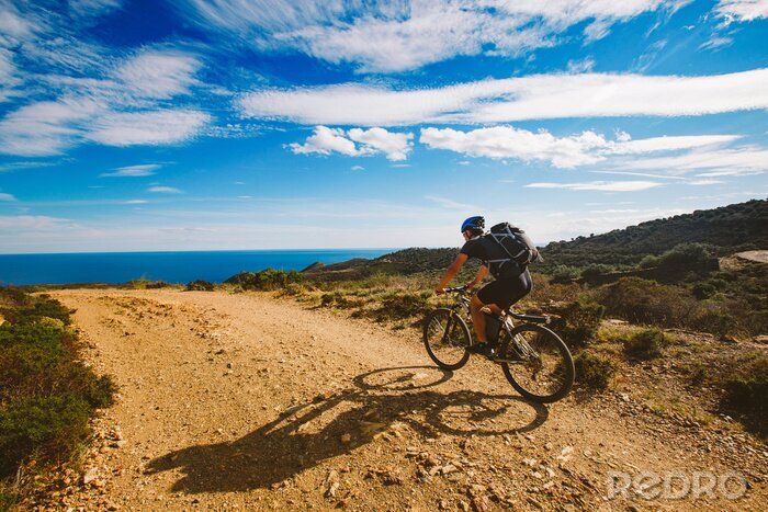 Canvas een jonge man die op een fietsroute in Spanje op een mountainbike rijdt tegen de achtergrond van de Middellandse Zee. Gekleed in een helm, een donkere en een zwarte rugzak