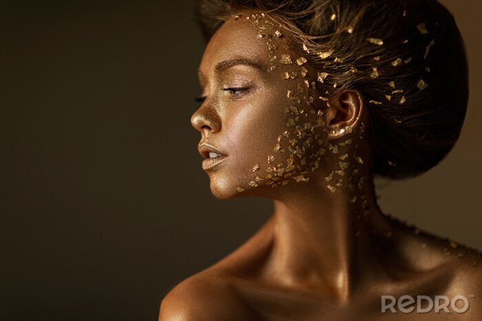 Canvas Fashion art portrait of model girl with holiday golden shiny professional makeup. beaty woman with gold metallic body and hair on dark background. Gold glowing skin. copy space