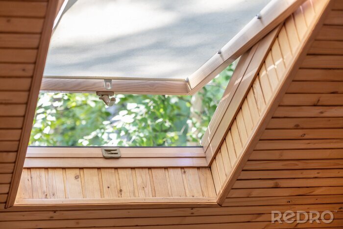 Canvas Geopend dakvenster met zonneblinden of gordijn in zolder. Kamer met schuin plafond gemaakt van natuurlijke eco-materialen en uitzicht op het park door een geopend raam. Milieuvriendelijk huis