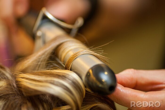 Canvas Hairdresser curling a blond woman's hair in professional hairdressing salon or barbershop , seen from behind the customer, unrecognizable.