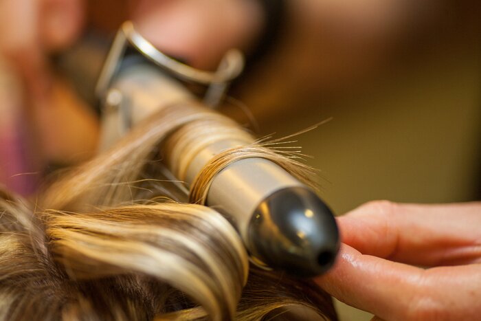 Canvas Hairdresser curling a blond woman's hair in professional hairdressing salon or barbershop , seen from behind the customer, unrecognizable.