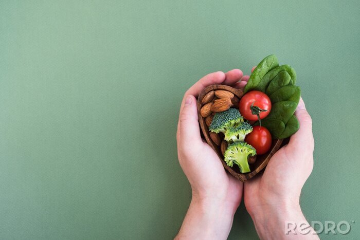 Canvas Healthy food for heart on green background. Man hands hold plate with vegetables, spinach and nuts. Diet, superfood and health concept. Top view, flat lay, copy space
