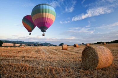 Canvas Hete luchtballons over hooibalen zonsondergang landschap