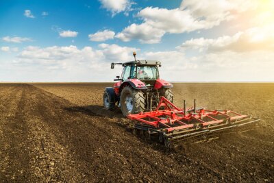 Landbouwer in tractor voorbereiding van grond met zaaibed cultivator als onderdeel van de pre zaaien activiteiten in het vroege voorjaar seizoen van de landbouw werken op landerijen.