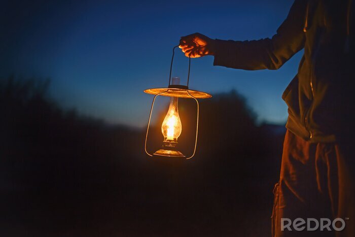 Canvas man die de oude lamp met een kaars buiten. hand houdt een grote lamp in het donker. oude lantaarn met een kaars verlicht de weg op een avond