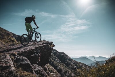 Canvas mountainbiker op een grote rots diep in de Alpen met zon en berg lagen achter