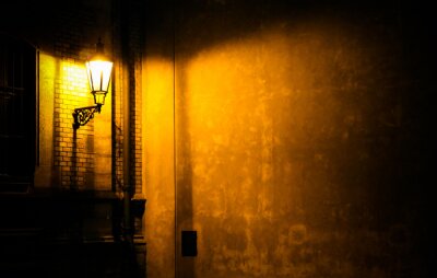 Canvas Oude lantaarn die een donkere muur van de steeghoek verlicht bij nacht in Praag, Tsjechische Republiek. Foto bijna monochroom met bruingele tinten van de lantaarn als lichtbron tegen de donkere schadu