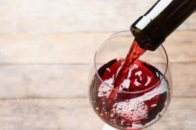 Canvas Pouring red wine from bottle into glass on blurred background, closeup. Space for text