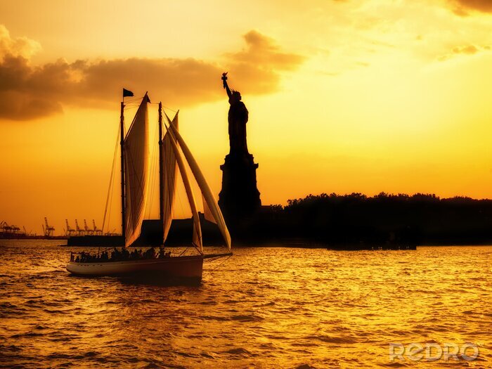 Canvas Silhouet van het Vrijheidsbeeld en een zeilboot bij zonsondergang