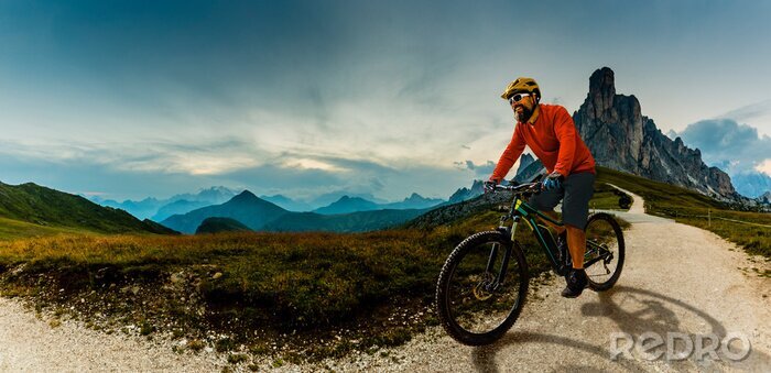 Canvas Single mountain bike rider on electric bike, e-mountainbike rides up mountain trail. Man riding on bike in Dolomites mountains landscape. Cycling e-mtb enduro trail track. Outdoor sport activity.