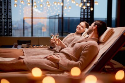 Canvas Spa, relax, enjoying concept. Married couple together relaxing in spa salon, lying on beds drinking champagne, using candles