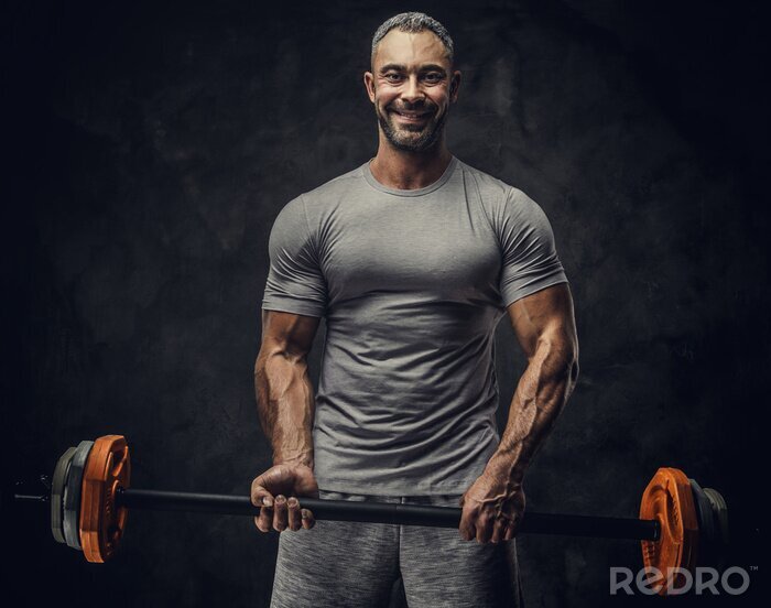 Canvas Strong, adult, fit muscular caucasian man coach posing for a photoshoot in a dark studio under the spotlight wearing grey sportswear, showing his muscles and holding a sport gear looking confident and