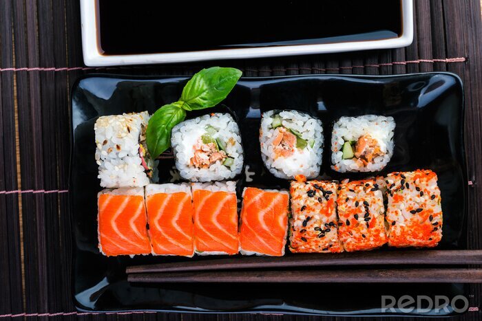 Canvas sushi rolt assortiment op de zwarte plaat en eetstokjes.