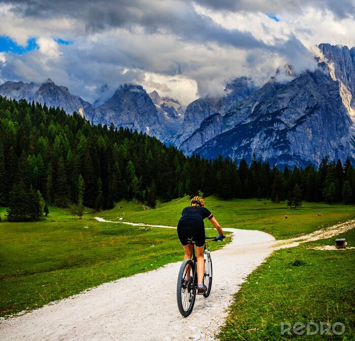 Canvas Tourist cycling in Cortina d'Ampezzo, stunning rocky mountains on the background. Woman riding MTB enduro flow trail. South Tyrol province of Italy, Dolomites.