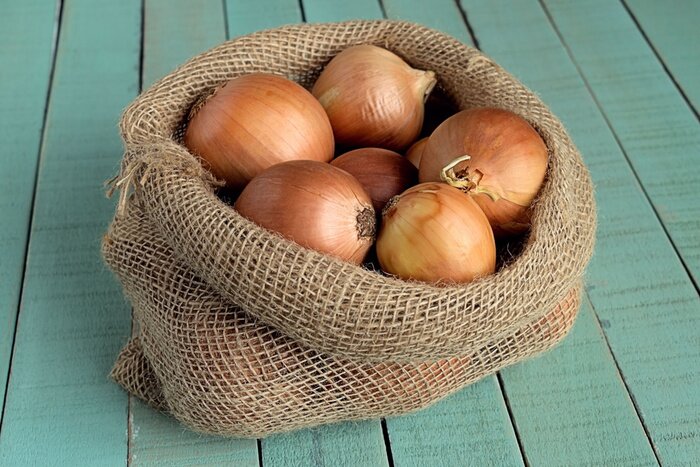 Canvas Uien. Zak met uien op een houten achtergrond.