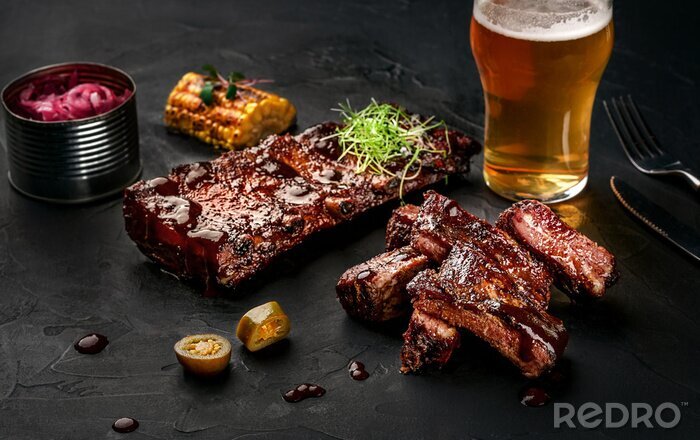 Canvas Varkensvleesribben in barbecuesaus en een glas bier op een zwarte leischotel. Een grote snack aan bier op een donkere steenachtergrond. Bovenaanzicht met kopie ruimte