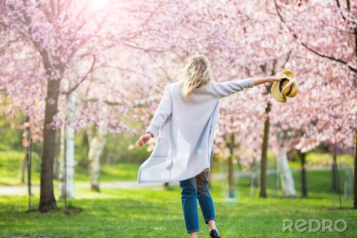 Canvas Young woman enjoying the nature in spring. Dancing, running and whirling in beautiful park with cherry trees in bloom. Happiness concept