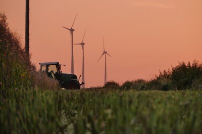 Fotobehang Beautiful shot of a tractor working in the fields with wind power plants in the background