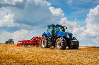Fotobehang Blue new tractor with red harrow in the field against a cloudy sky, agricultural machinery work