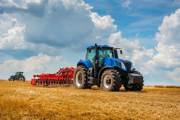 Fotobehang Blue new tractor with red harrow in the field against a cloudy sky, agricultural machinery work