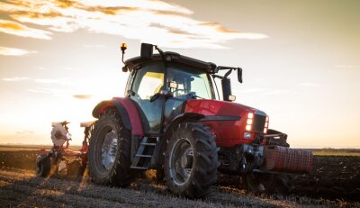 Boer ploegen stoppelveld met rode tractor bij zonsondergang