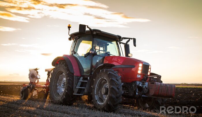 Fotobehang Boer ploegen stoppelveld met rode tractor bij zonsondergang