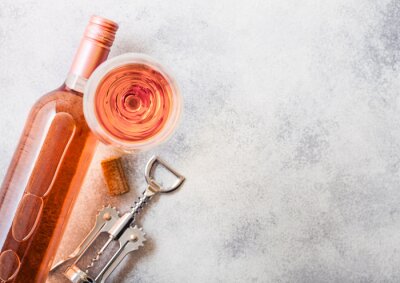 Bottle and glasses of pink rose wine with cork and corkscrew opener on stone kitchen table background. Top view. Space for text