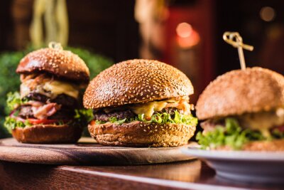 Fotobehang Drie sappige smakelijke hamburger op de witte plaat op een donkere achtergrond