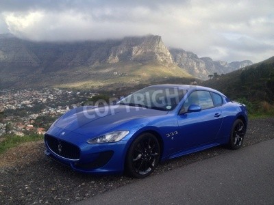 Fotobehang Een blauwe Maserati met een berglandschap op de achtergrond