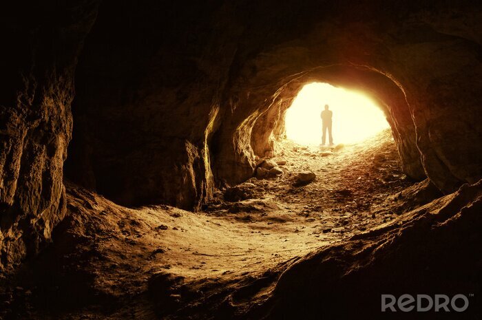 Fotobehang Een man bij de ingang van een verlichte grot