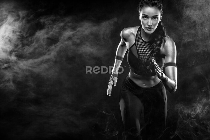 Fotobehang Een sterke atletische, vrouwensprinter, die op zwarte achtergrond loopt die in de sportkleding, fitness en sportmotivatie draagt. Runner concept met kopie ruimte.