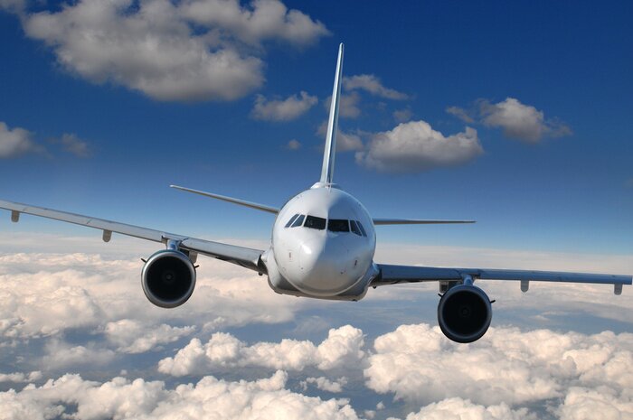 Fotobehang Een vliegtuig dat op een heldere dag boven de wolken vliegt