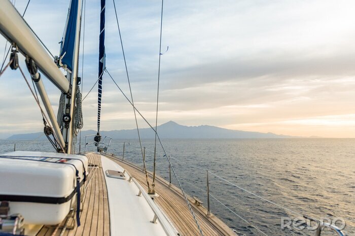 Fotobehang Een zeilboot op zee in de stralen van de ondergaande zon.