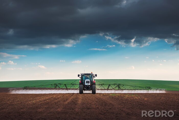 Fotobehang Farming tractor plowing and spraying on field