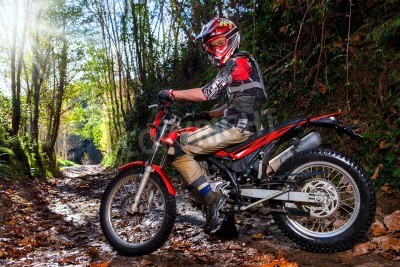 Fotobehang Full length portrait of motocross rider sitting on motorbike in woods.