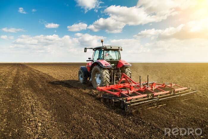 Fotobehang Landbouwer in tractor voorbereiding van grond met zaaibed cultivator als onderdeel van de pre zaaien activiteiten in het vroege voorjaar seizoen van de landbouw werken op landerijen.